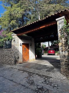 a red car is parked in front of a stone building with a wooden door and awning