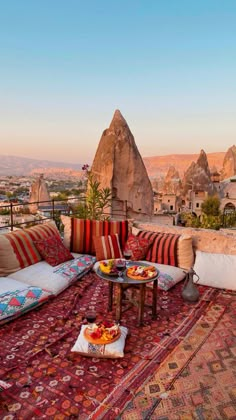 an outdoor seating area on top of a building with mountains in the background and colorful pillows