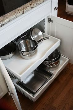 an open drawer with pots and pans on it in the corner of a kitchen