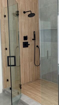 a walk in shower sitting next to a wooden floor and wall with a glass door