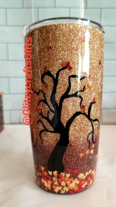 a coffee cup with a tree painted on the side and gold flakes around it