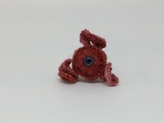 a crocheted red stuffed animal sitting on top of a white table next to a blue eye