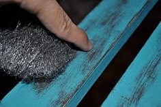 a person's hand touching the top of a blue bench with metal wire on it