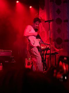 a man standing on top of a stage next to a microphone and keyboard in front of a red light