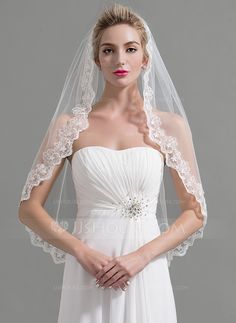 a woman wearing a white wedding veil with an applique on the top and shoulder