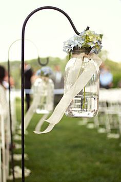 an outdoor ceremony with chairs and flowers in mason jars hanging from the back of the aisle