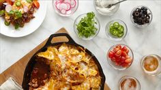 a skillet filled with mexican food next to bowls of salads and condiments