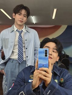 a man taking a selfie with his cell phone in front of him and another person behind him