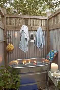 a bath tub sitting next to a wooden fence with candles on the side and towels hanging from it