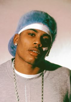 a man wearing a blue hat and silver necklace with a chain around his neck is looking at the camera