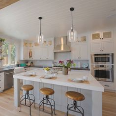 a large kitchen with white cabinets and wooden stools in front of an island counter