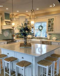 a large kitchen island with stools in front of it and lights hanging from the ceiling