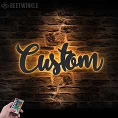 a person holding a cell phone in front of a brick wall with the word custom on it