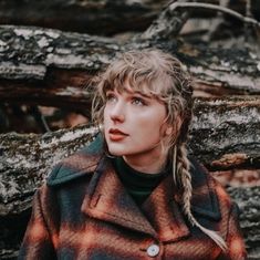 a woman with braids standing in front of a tree trunk and looking off into the distance