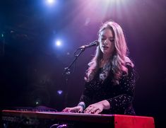 a woman standing at a keyboard in front of a microphone on stage with lights behind her