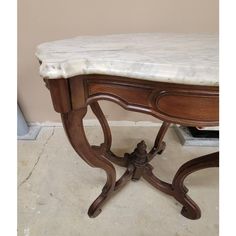 an old wooden table with marble top in a room next to a wall and floor