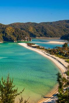 an aerial view of the water and beach in front of some hills with trees on it