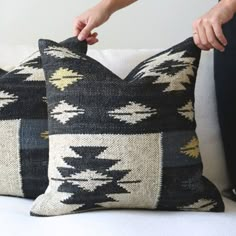 two black and white pillows being held up by someone's hand on a couch