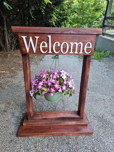 a welcome sign with purple flowers hanging from it's sides on a wooden stand