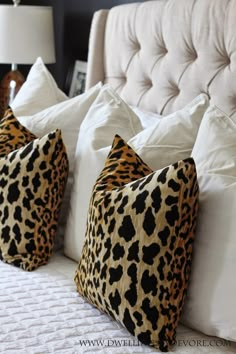 two leopard print pillows sitting on top of a bed next to white sheets and pillows