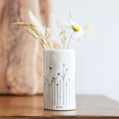 a white vase with flowers in it sitting on a wooden table next to a wall