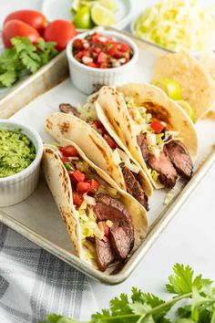 three steak tacos on a tray with guacamole and salsa