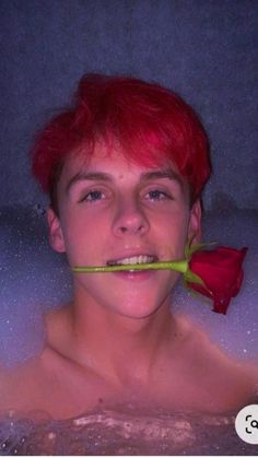 a young man with red hair in a hot tub holding a rose to his mouth