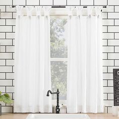 a kitchen sink sitting under a window next to a white tiled wall with a black faucet