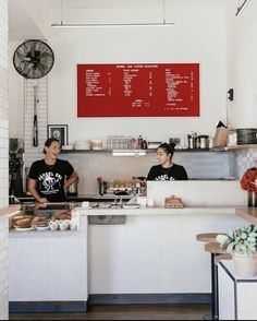 two people sitting at a counter in a small restaurant with food on the counter and signs above them