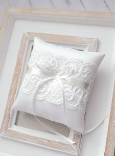 a white wedding ring pillow in a wooden frame with a ribbon on the front and side