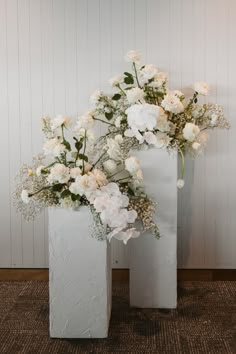 two white vases with flowers in them sitting on the floor next to each other