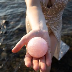 a person holding a pink ball in their hand near the water's edge, while wearing a sparky dress