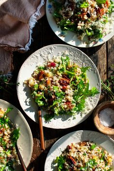 three white plates filled with salad on top of a wooden table next to utensils