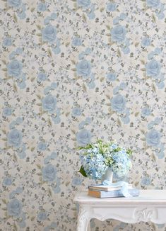 a white table topped with blue flowers next to a wallpaper covered in floral designs