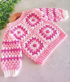 a pink and white sweater sitting on top of a table next to a potted plant