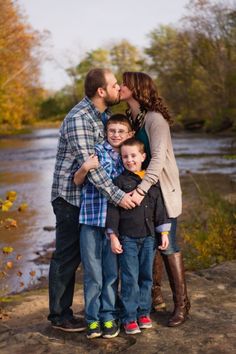 a family kissing each other while standing in front of a river