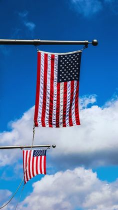 two american flags hanging from a metal pole in front of a blue sky with clouds