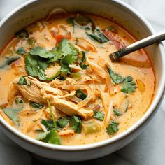 a white bowl filled with chicken noodle soup and garnished with cilantro