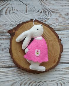 a white stuffed animal in a pink dress on top of a tree stump with a string