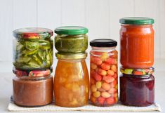 several jars filled with different types of vegetables and sauces on top of a cloth