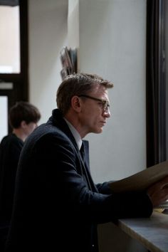 a man sitting at a table looking out the window while holding a piece of paper