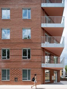 a woman walking past a tall brick building with balconies on the top floor