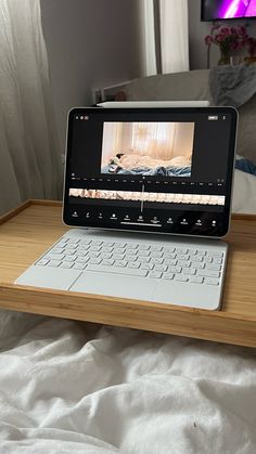 an open laptop computer sitting on top of a wooden table next to a bed with white sheets