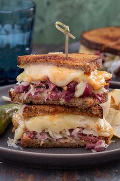 two sandwiches stacked on top of each other with pickles next to them and another sandwich in the background