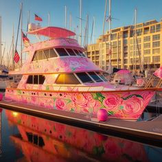 a large pink boat is docked in the water with other boats and buildings behind it