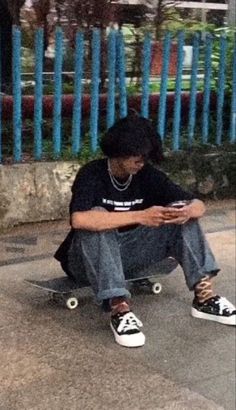 a man sitting on top of a skateboard while looking at his cell phone in front of him