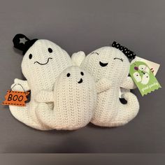 three white knitted ghost stuffed animals sitting next to each other on a gray surface