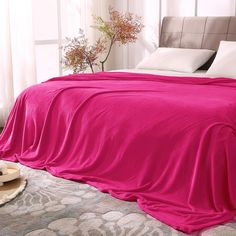 a bed covered in a pink blanket next to a vase with flowers on top of it