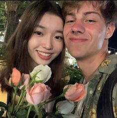 a young man and woman are posing for a photo with roses in front of them