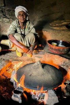 a woman sitting in front of an open fire with pots and pans on it